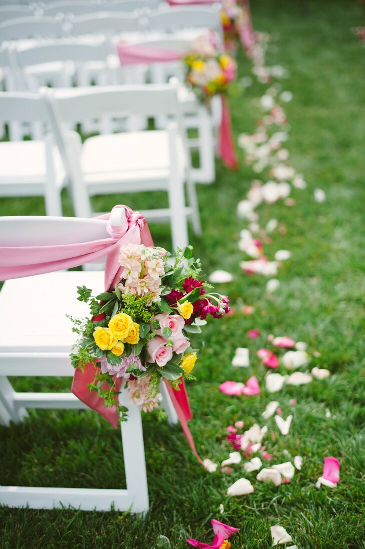 At the outdoor ceremony, white folding chairs arranged into rows had a mix of colorful roses, hydrangeas and greenery, blending well with the beautiful pink ribbon draped on the back.