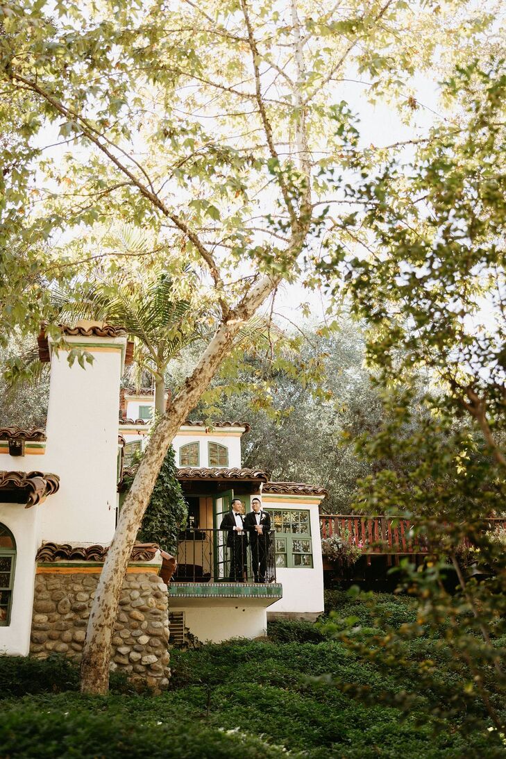 Grooms on a Balcony Overlooking Reception at Spanish-Style Villa at Their Venue