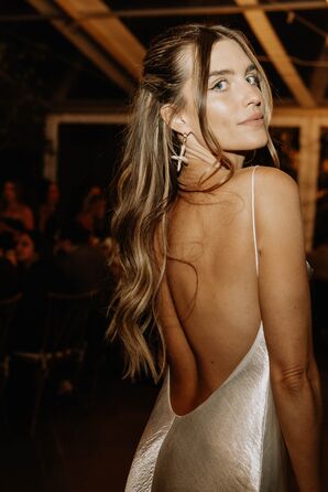 Stylistic Photo of Bride in Modern Makeup, Low-Back Reception Dress, Oversized Cross Earrings