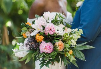A couple stand together, holding an overflowing and vibrant peony bouquet.