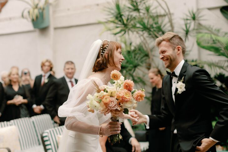 Bride With Light Bouquet of Coral, Blush and White Flowers, Pearl Headband Smiling With Groom in Tux