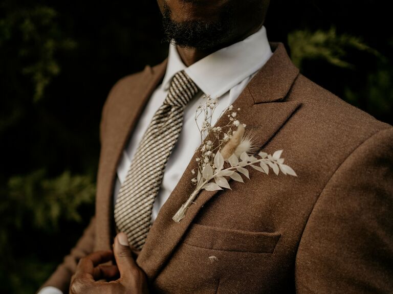 2023 wedding color trend groom wearing brown tweed suit with dried flower wedding boutonniere and checkered tie