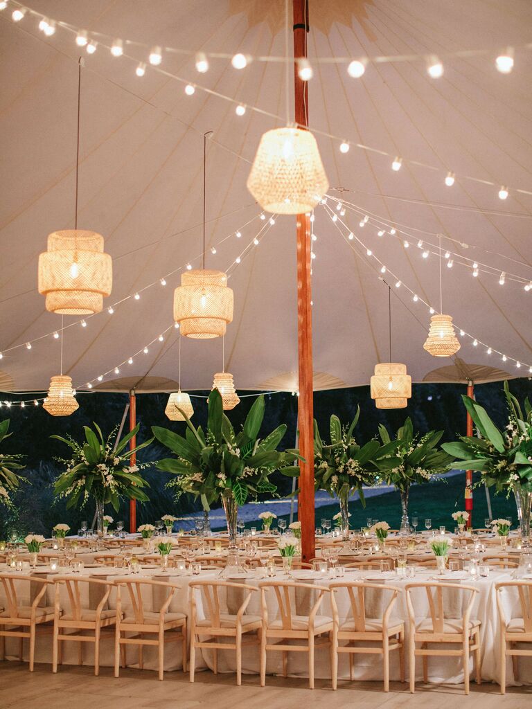tented wedding reception with bistro string lights and mismatched rattan lanterns hanging above banquet tables