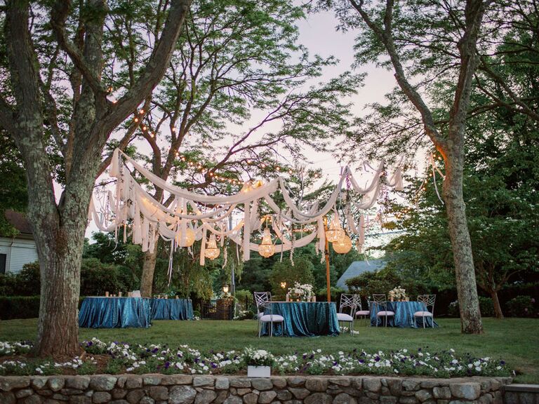 White drapes hanging from trees at backyard summer wedding