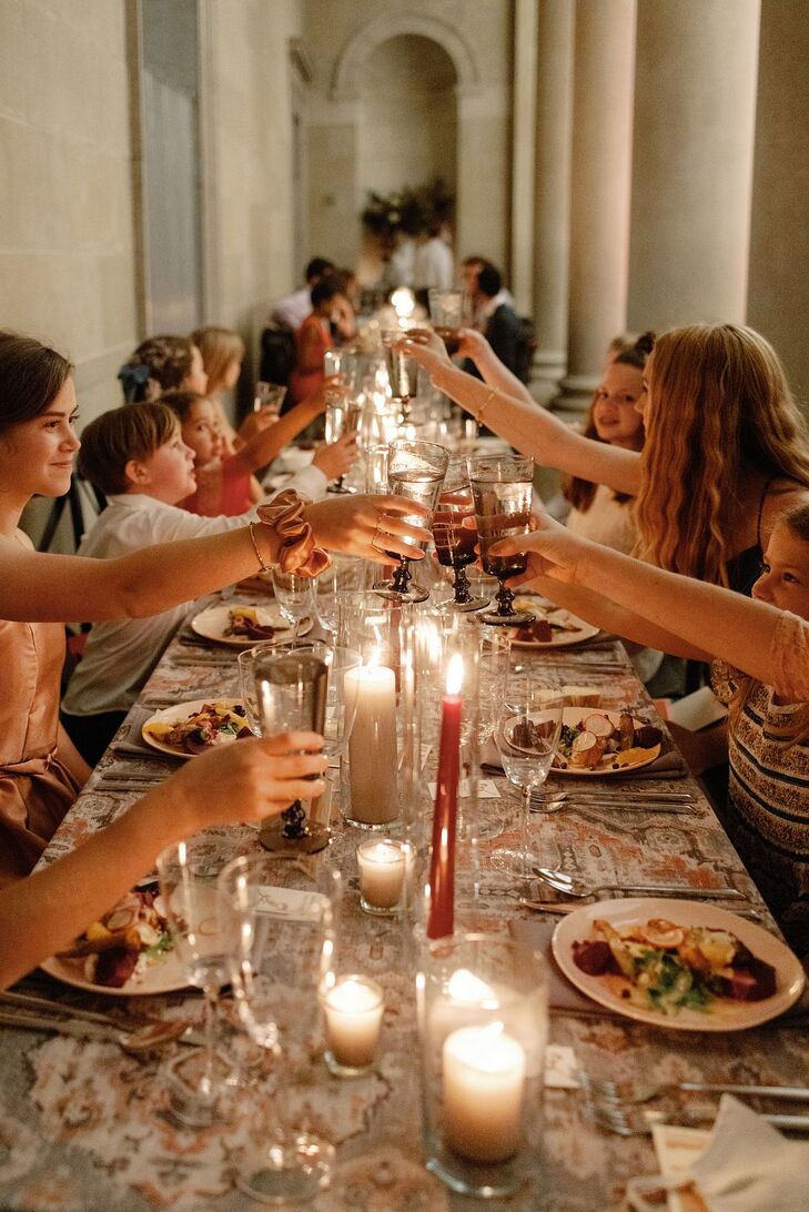 Guests Cheers Glasses Over Long Reception Table With Candles in Museum
