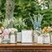 A bespoke flower bar seating chart with framed table guest lists and calligraphy, on varying vases featuring bright pastel flowers like peonies and garden roses in pink, blush, blue, coral, white, yellow and purple at a garden party themed wedding reception on an estate lawn