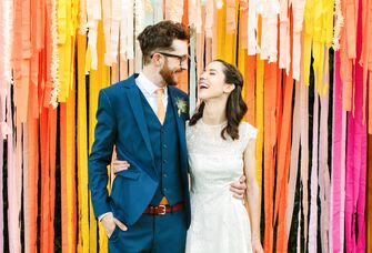 Couple laughs while standing in front of colorful streamers. 