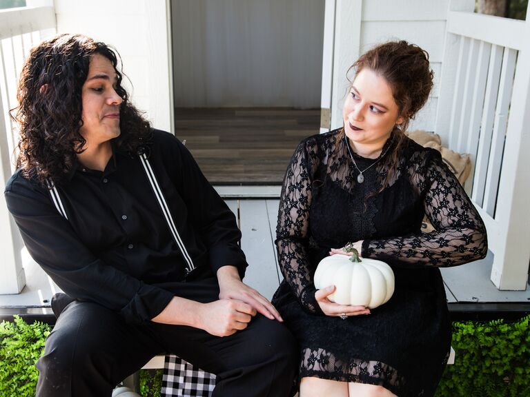 Couple wearing black clothing pose for the camera with a white pumpkin. 