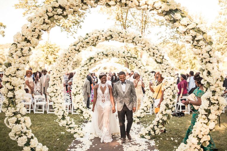Couple exiting wedding ceremony under white floral arches