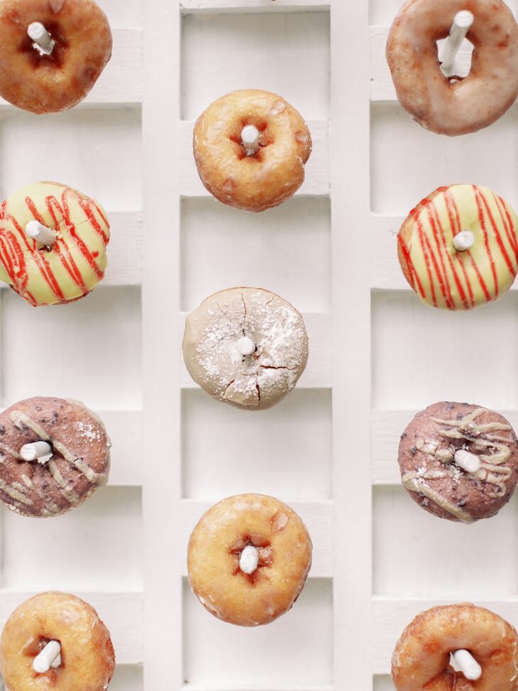 A bride and groom's fun donut wall at their garden party wedding featuring different colors, designs, and flavors for guests to enjoy as dessert.