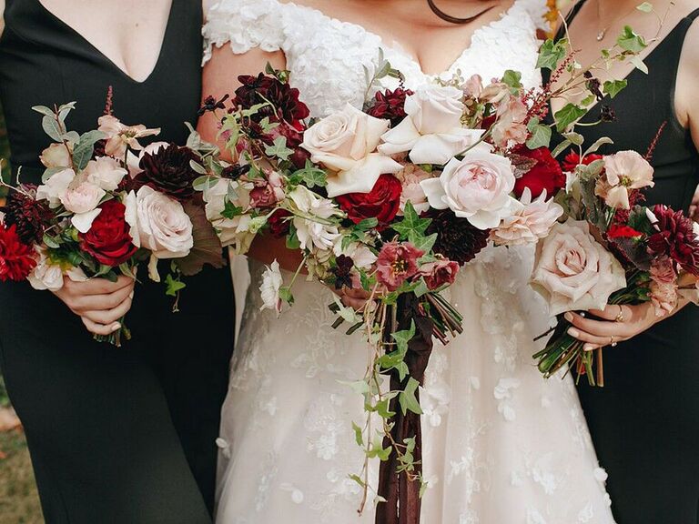 Bride with bridesmaids holding red and ivory bouquets at fall wedding