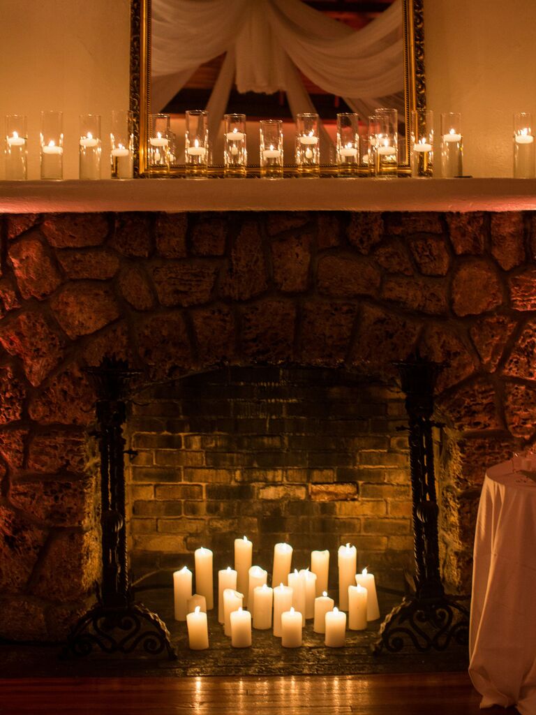 stone wedding fireplace decorated with white pillar candles and floating candles in glass vases