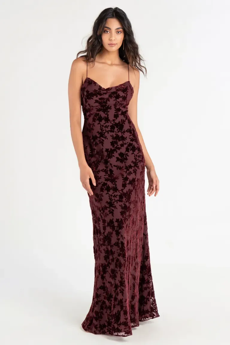 Model wears a wine-colored spaghetti strap dress with floral detailing. 