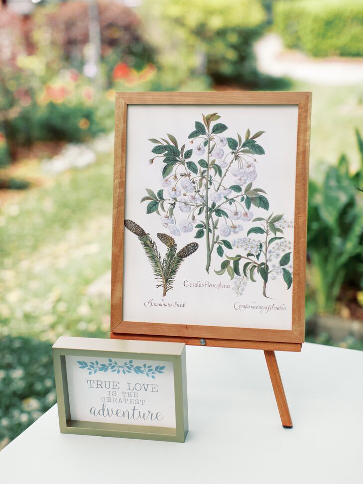 A beautiful floral design featuring different types of flowers, accented with the saying, "true love is the greatest adventure" at a couple's garden party wedding.