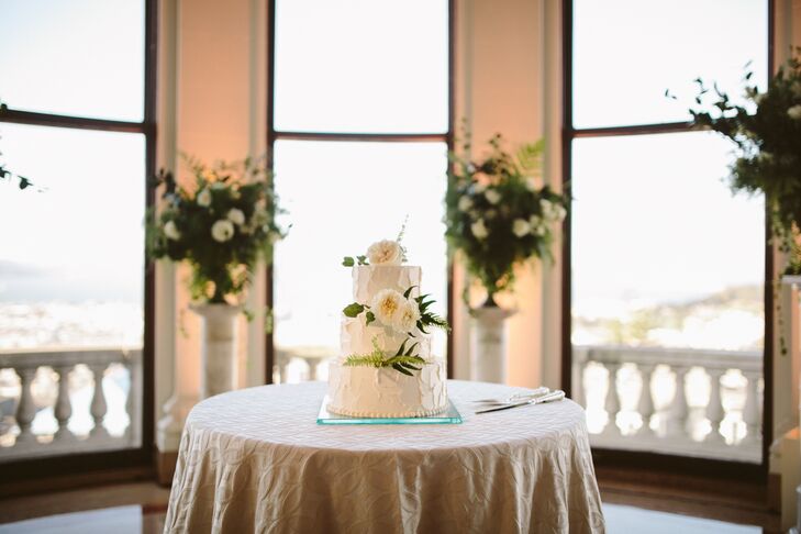 The three-tier ivory wedding cake was positioned on top of an ivory-dressed table at the reception. Accents of fern and ivory roses accented each layer, and an elegant serving set was positioned nearby for the couple to use.