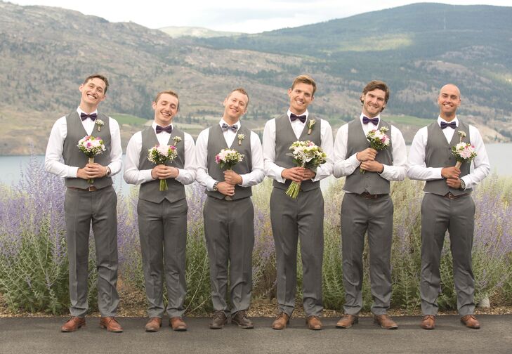The groomsmen and groom carried the bride and bridesmaid bouquets for this charming wedding party picture. The groomsmen wore gray suits with eggplant purple bow ties.