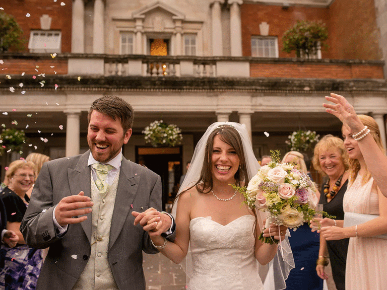 Bride and groom smiling during recessional while guests throw flowers. 