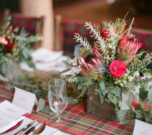 winter wedding centerpiece with red and green plaid table runner and red and green flowers in wooden square vase