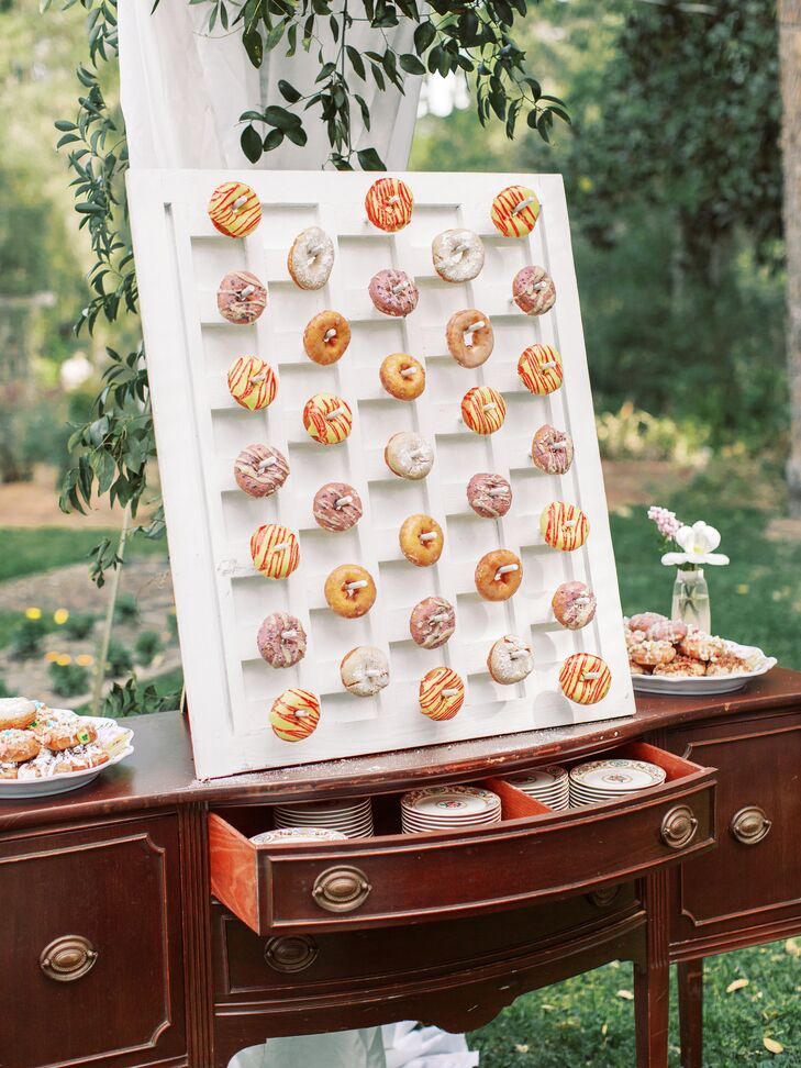 A bride and groom's vintage dessert table featuring a donut wall and extra treats at their garden party wedding.
