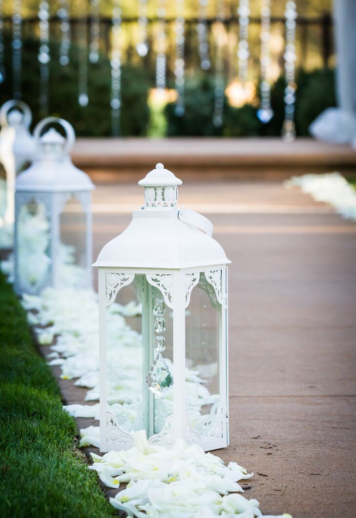 At the outdoor ceremony, the aisle was lined on both sides with white petals and tall elegant lanterns. This led to the wedding arch, which was draped with white linens and dangling crystals hanging down the middle.