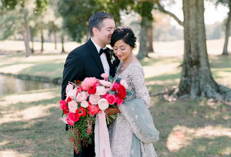 A couple pose together with a gorgeous red and white anemone bouquet.