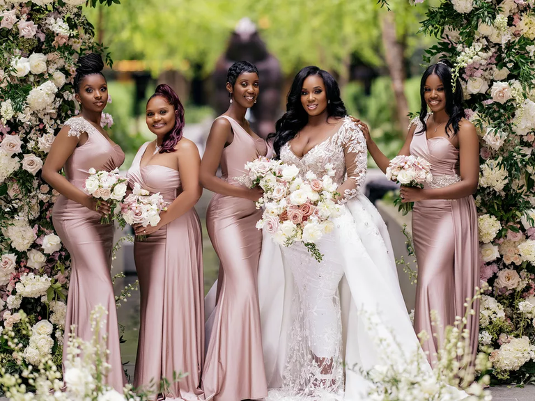 A bride and her bridesmaids pose for a photo, the wedding party wearing dusty rose gowns.