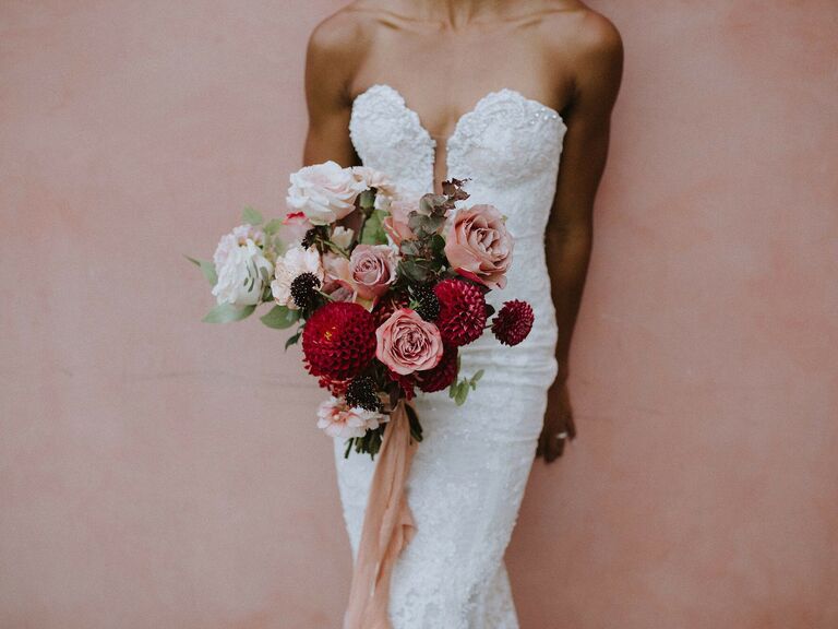 Bride holds a bouquet featuring stunning red dahlias and blush pink roses. 