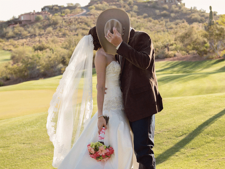 Bride and groom kissing behind a cowboy hat. 