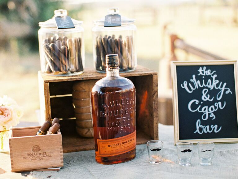 A whiskey bottle and bars of cigars sit on a table to be enjoyed by wedding guests. 
