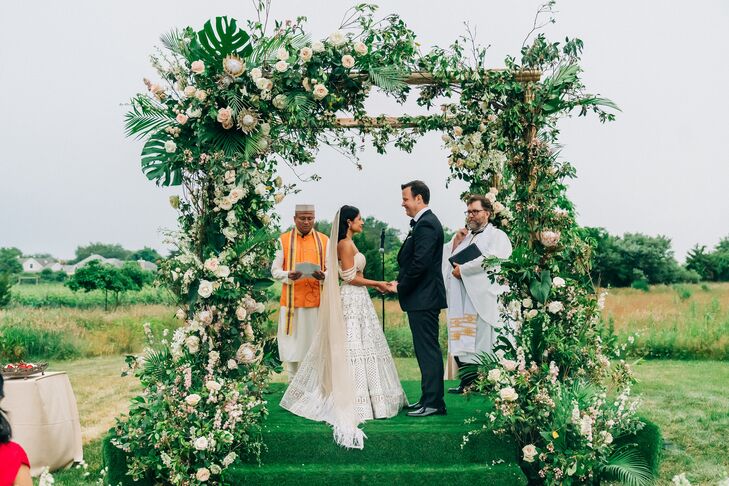 Bride and Groom During Vows Underneath Wedding Arch and Floral Arrangements