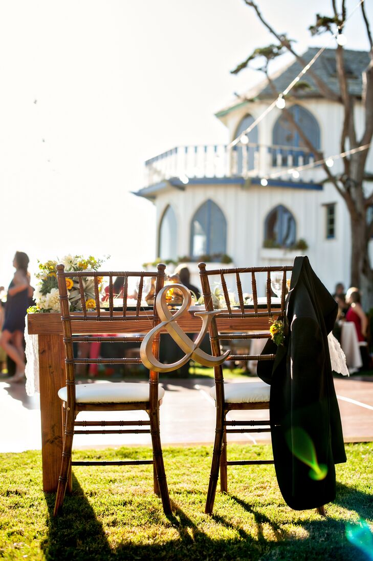 The bride and groom chose custom unfinished wooden chairs decorated with a lighter wooden ampersand for their oceanside reception to play up their rustic outdoor theme.