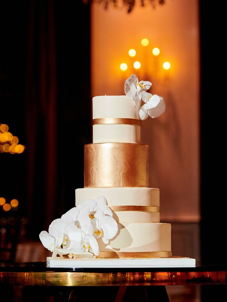 four tier fondant wedding cake with metallic gold foil stripes and white orchids