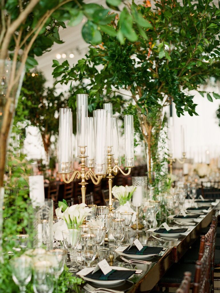 tall wedding centerpiece featuring gold candelabras with glass covers and greenery branches in vases