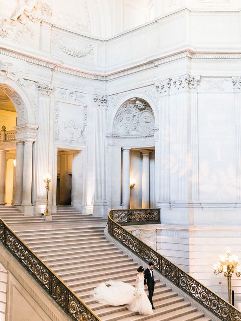 Bride and groom walking down opulent steps at regencycore wedding venue