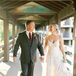 Bride in a Fitted A-Line Dress and Groom in Dark Gray Suit Hold Hands