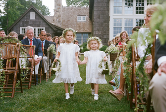 Two flower girls walk hand in hand down an aisle at this outdoor wedding.