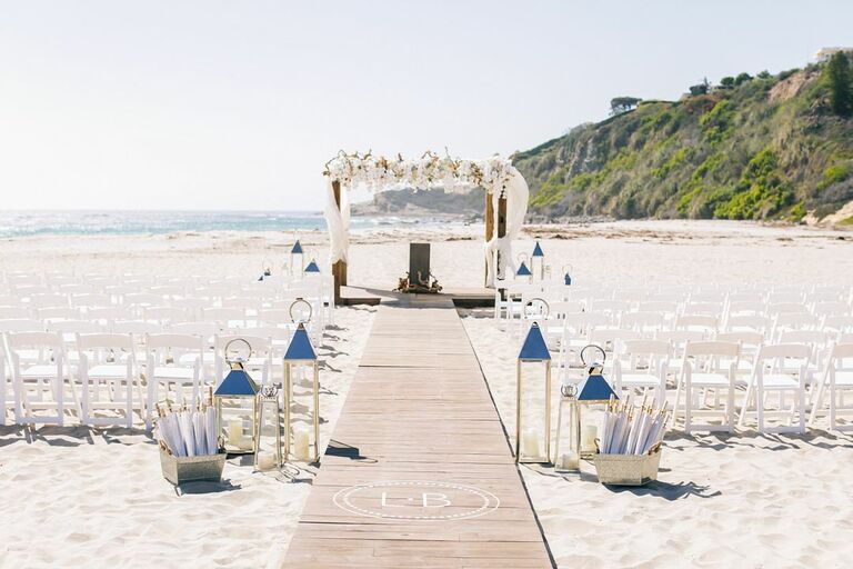 Beach wedding ceremony with white folding chairs, wood walkway and romantic arch