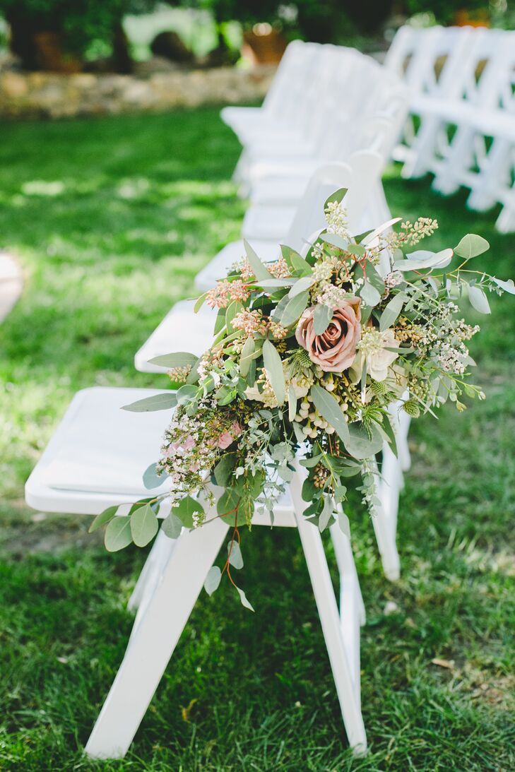 At the ceremony, white folding chairs that lined the aisle had overflowing flower arrangements filled with roses, eucalyptus and leafy greens—contributing to the overall garden-inspired theme of the day.