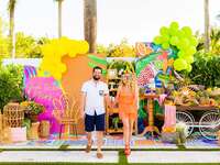 man and woman walking hand in hand in front of a bright balloon backdrop