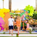 man and woman walking hand in hand in front of a bright balloon backdrop