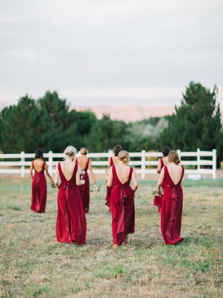 bridesmaids walking through field wearing long red dresses