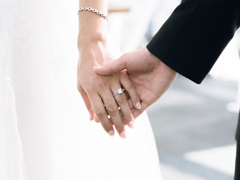 Bride holding hands with groom showing off engagement ring on wedding day