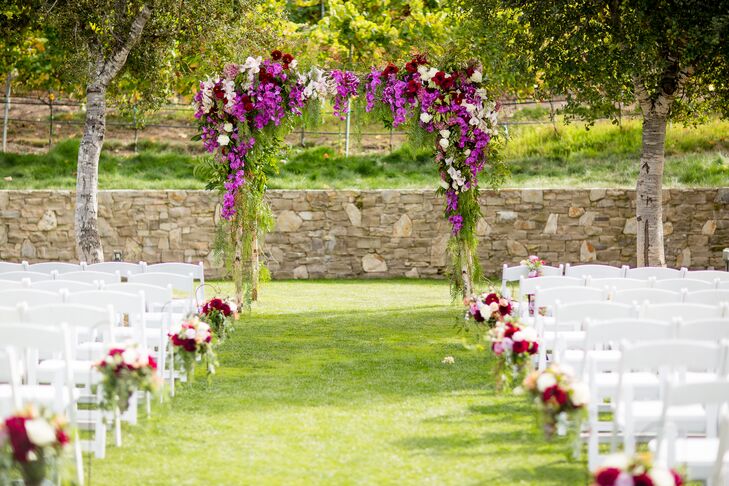 Laura and Pierre married under a colorful arch decorated with lush greenery, rosehips, pepperberries, hydrangeas, dahlias, roses and vibrant purple orchids.