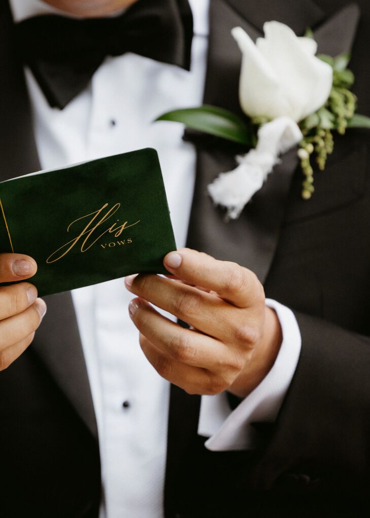 Groom in Classic Tuxedo Holding an Emerald Green Vow Book With Gold Writing