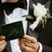 Groom in Classic Tuxedo Holding an Emerald Green Vow Book With Gold Writing