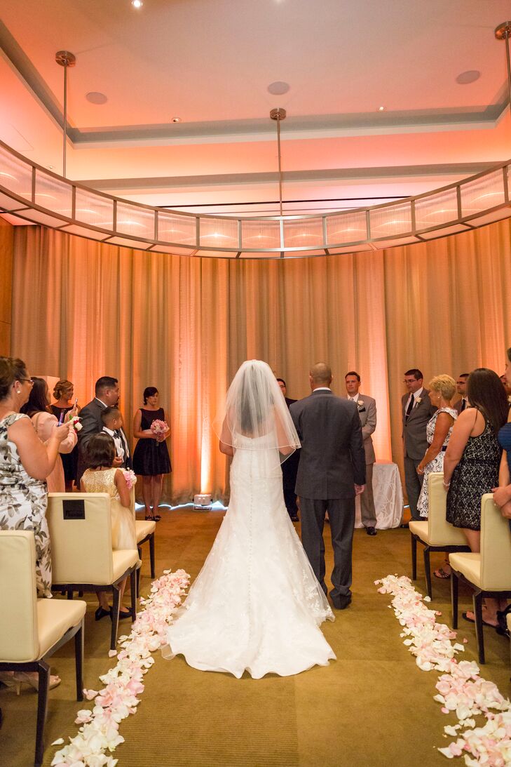 White and pink flower petals lined the aisle at the indoor reception as the room was illuminated with blush pink lighting.