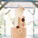 Grooms in Black and Gray Tuxedos Cut a Five-Tier White and Silver Wedding Cake on Hanging, Suspended Cake Stand at Museum Wedding