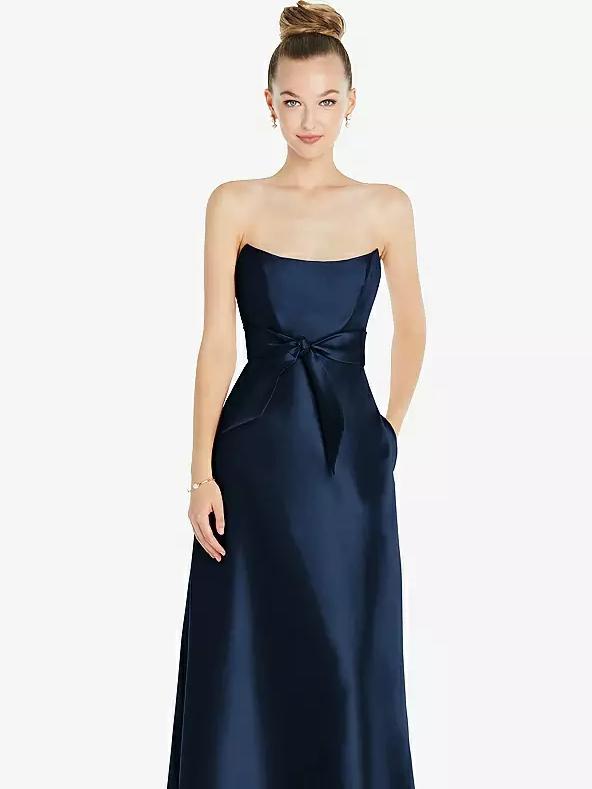 A model shows off a dark strapless dress with a bow at the waist.