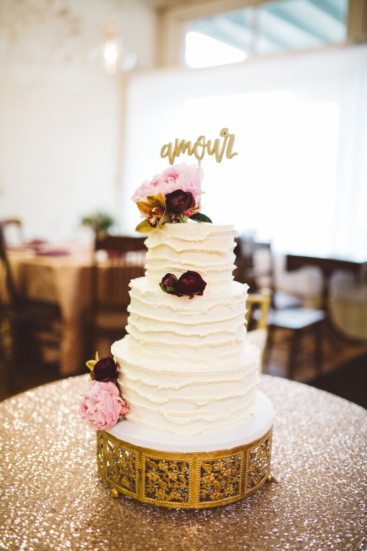 Morgan and Stanley's wedding cake honored family traditions, incorporating flavors like red velvet, carrot and apple butter for each layer of the cake’s three tiers. The decadent confection was iced in ivory buttercream and finished with pink peonies, burgundy roses and a vintage gold-tipped topper spelling "amour," a nod to Stanley’s Haitian roots.