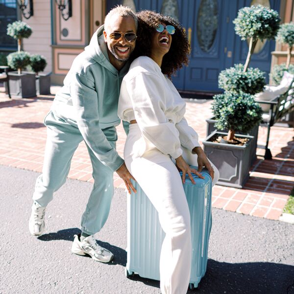 A couple laugh and smile while posing as if riding on their color-coordinated luggage.